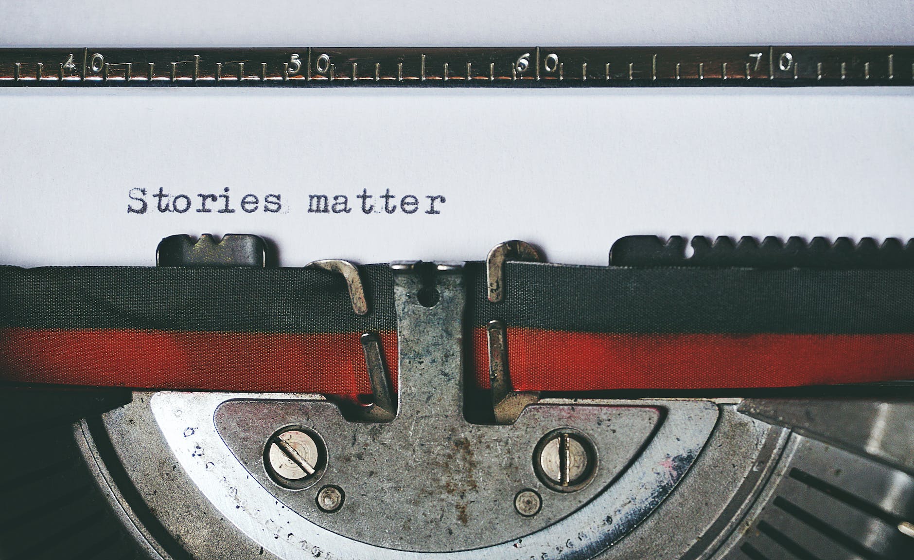 Close up of a mechanical type writer, a white piece of paper is in it and the words: stories matter are written on the paper