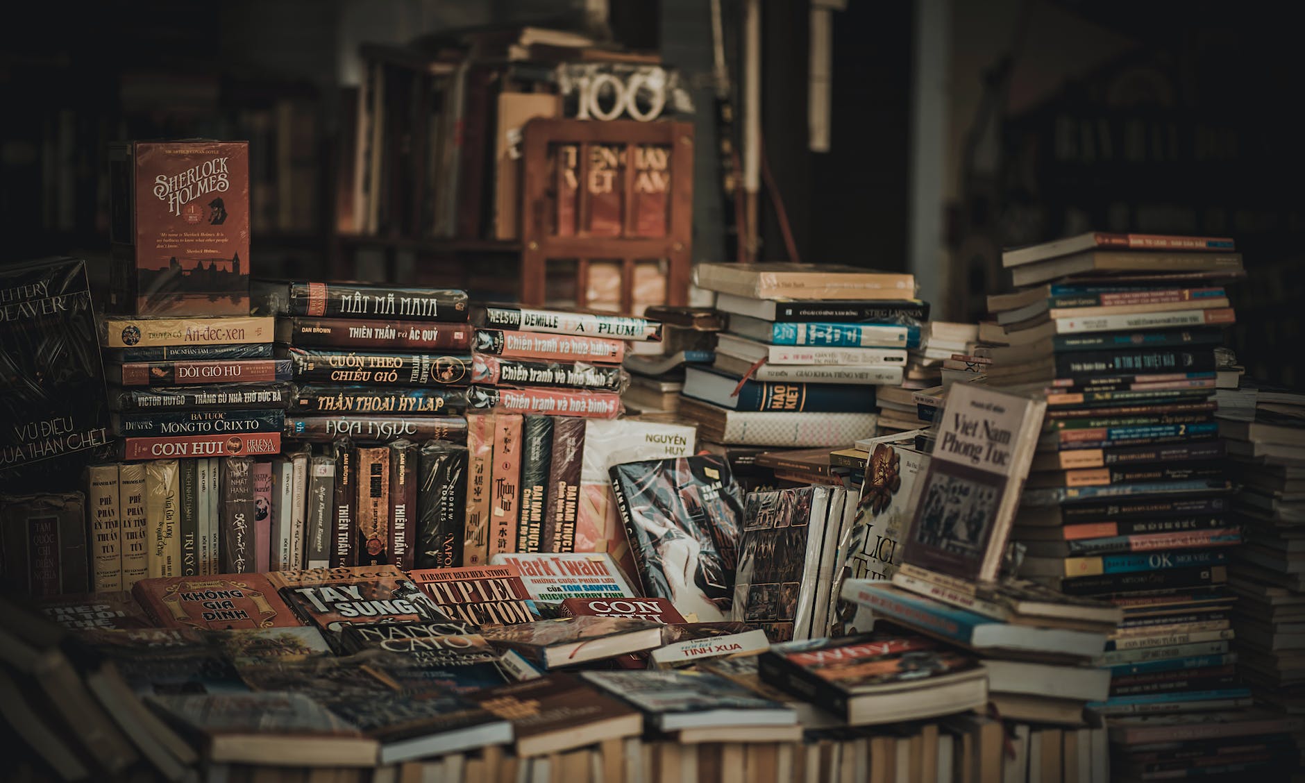 This is a close up of a tumbled pile of books, it could be from a market stall or maybe from within a second hand book store. The image colouring is sepia with light highlighting the centre of the image
