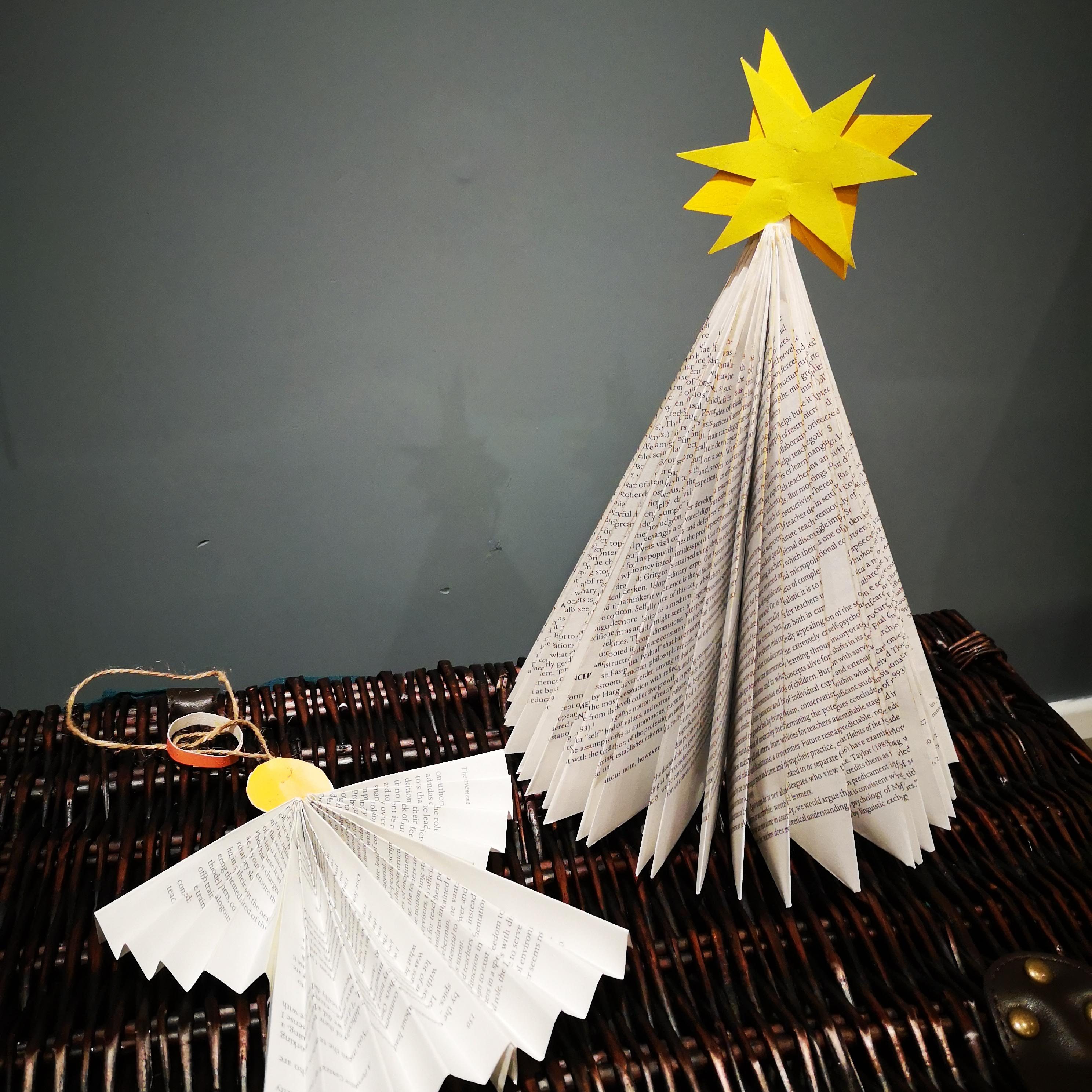 A christmas tree folded out of an old book, and a paper angel made from the same book on top of a hamper. The tree has a yellow star on top