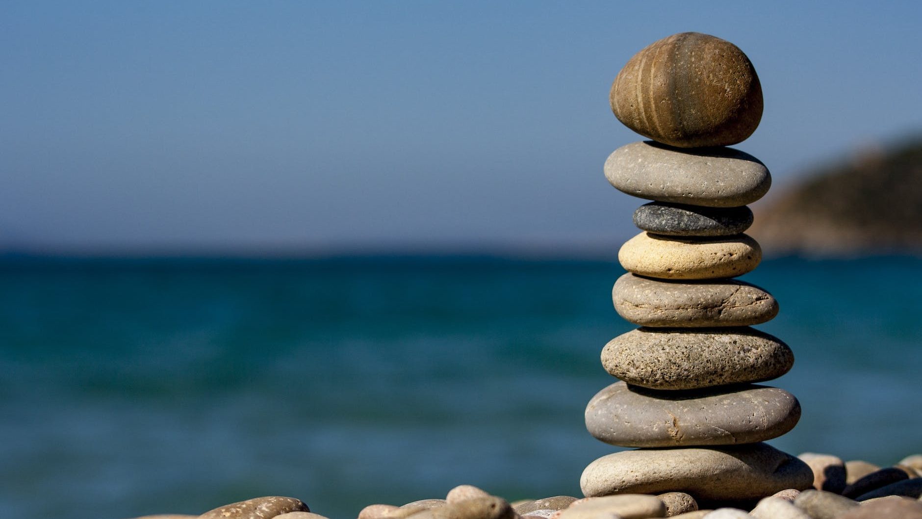 close up of a pile of a mini tower of pebbles the blurred ocean and blue sky are in the background